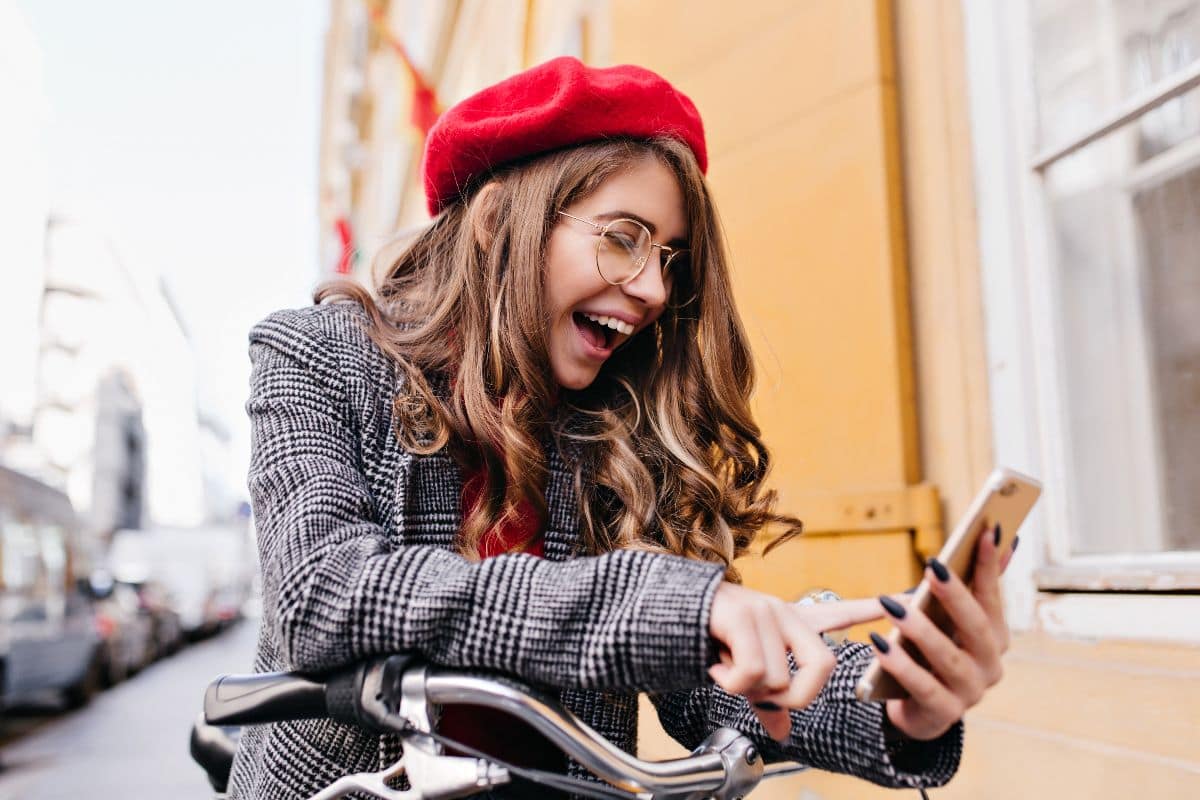 Femme à chapeau rouge et smartphone, crie de joie devant le tarif discount du 100 Go en 5G de Syma à moins de 8€/mois